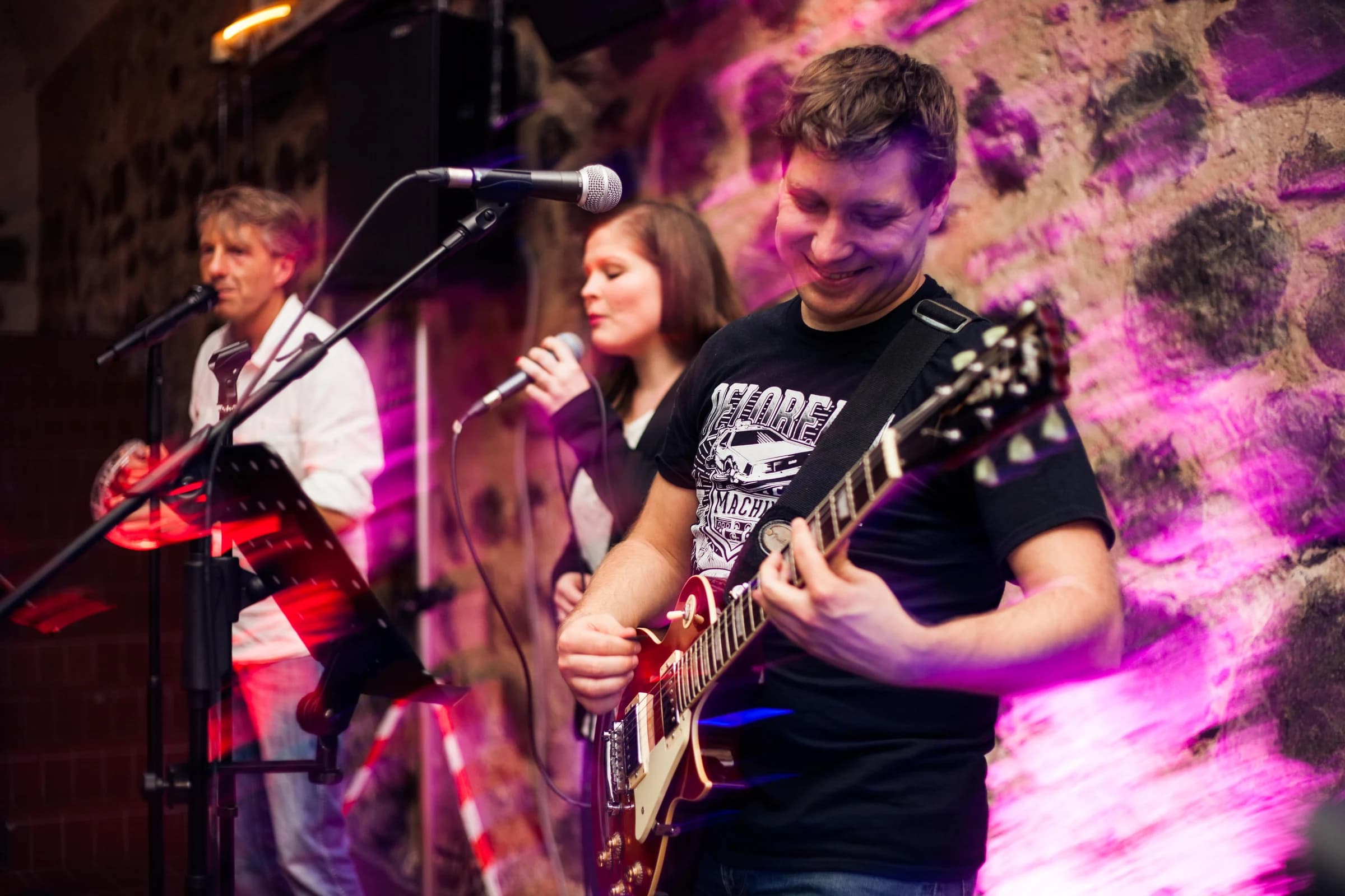 Band mit Gesang und Gitarre im farbigen Licht vor einer Steinwand