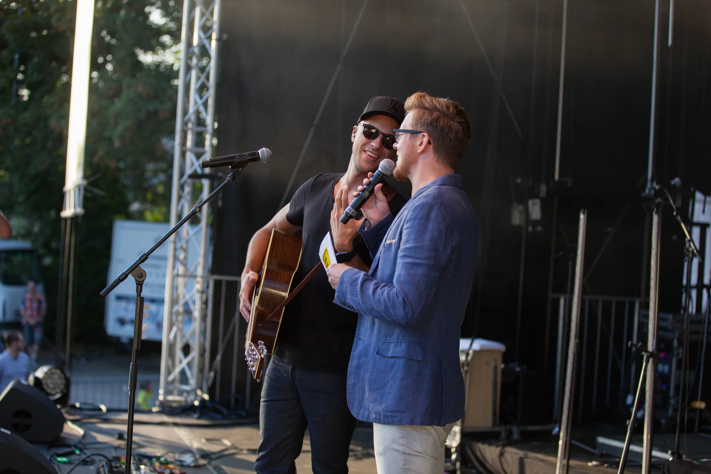 Zwei Künstler mit Mikrofon und Gitarre auf einer Open-Air-Bühne
