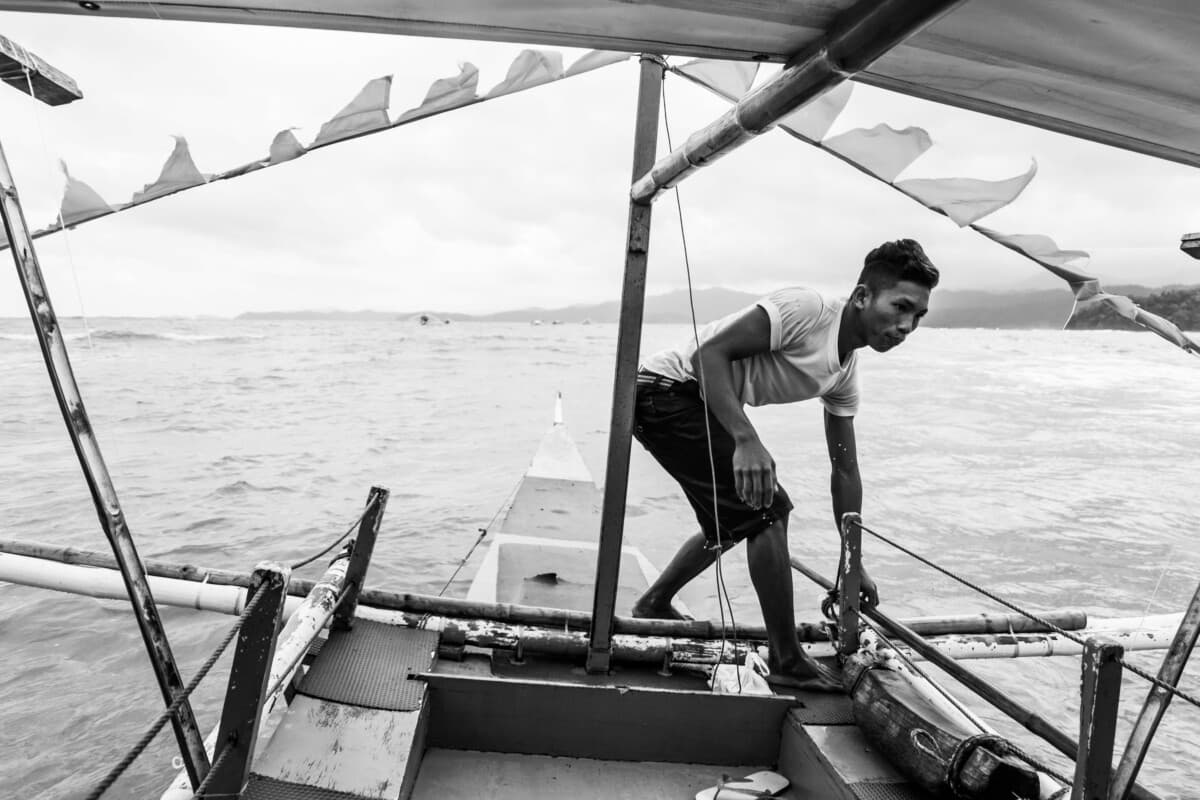 Black-and-white documentary photograph of a man working on a small boat