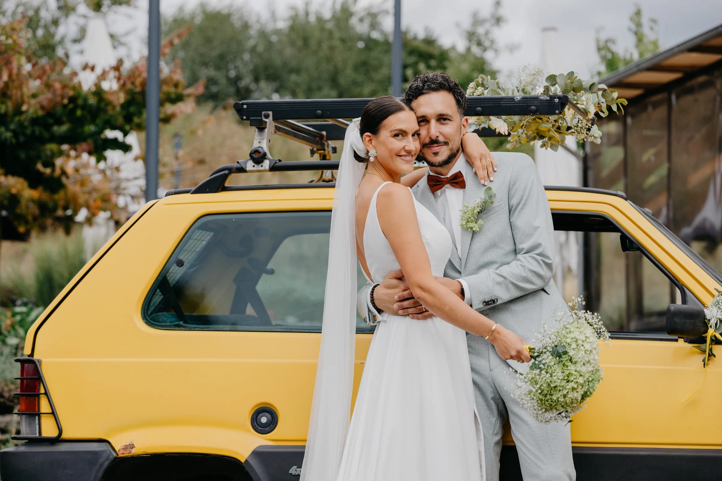 A wedding couple embracing beside a yellow vintage car